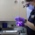 Dental Work A female military dental officer, identifiable by her navy blue uniform and name tag, is examining or preparing a dental instrument under UV/blue light in what appears to be a shipboard or military dental clinic. She is wearing full personal protective equipment including a surgical mask, magnifying loupes, and purple nitrile gloves. A dental instrument tray with tools is visible in the foreground.