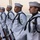 170117-N-BL637-018 A formation of U.S. Navy sailors in dress white uniforms stand at attention on the deck of a naval vessel, holding rifles with fixed bayonets. They appear to be participating in a formal ceremonial detail, likely a burial at sea or honors ceremony, given the solemn posture and ceremonial aiguillettes. The image is taken at dusk or dawn with the ocean visible in the background.