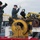 170113-N-GS192-015 A group of U.S. Navy sailors in digital camouflage (NWU Type I) uniforms are working on the deck of a naval vessel, operating or signaling around large yellow mechanical winch/capstan equipment. The personnel are wearing cold-weather gear including black watch caps and gloves, suggesting operations in a cold climate. The background shows a waterfront facility with multi-story buildings, consistent with a naval base or shipyard.