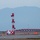 Lightning II strikes Iwakuni, F-35B arrives A military jet aircraft, likely an F-22 or F-35, is captured on final approach to land at a military airfield during dusk or early evening. The runway is equipped with standard approach lighting systems including a prominent red-and-white MALSR (Medium Intensity Approach Lighting System with Runway Alignment Indicator Lights) tower and crossbar array. An ILS (Instrument Landing System) sign is visible on the taxiway, indicating a fully instrumented runway.