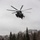 HMH-464 Marines Conduct Flight Operations during Exercise Frigid Condor A large military helicopter, identifiable by the number '59' on its fuselage, is captured hovering or flying low over a snow-covered clearing. The aircraft appears to be a heavy-lift helicopter, consistent with a CH-53E Super Stallion used by the U.S. Marine Corps. The winter setting features a mixed forest of evergreen and bare deciduous trees under an overcast sky.