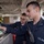 170123-N-PP996-053 Two U.S. Navy sailors are operating a touchscreen control panel aboard a naval vessel. The sailor in the foreground is wearing a radio and ear protection, actively interacting with the display, while a second sailor observes from behind. The setting appears to be an interior compartment of a warship.