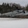 HMH-464 Marines Conduct Flight Operations during Exercise Frigid Condor A U.S. Marines CH-53E Super Stallion heavy-lift helicopter assigned to HMH-464 is captured hovering low over a snow-covered field. The aircraft bears the side number '57' and tail code 'EN' with a shamrock insignia, indicating it belongs to Marine Heavy Helicopter Squadron 464. The setting appears to be a winter woodland environment, likely during a cold-weather training exercise.