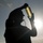 170117-N-PP996-044 A silhouetted worker wearing a hard hat and headset holds a cylindrical glass jar or sample container up toward the sun, backlighting it for visual inspection. The image is taken against a bright sky with sun flare, creating a dramatic silhouette effect. The setting appears to be an outdoor industrial or maritime environment.