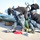 Expeditionary ordnance loading exercise Military personnel in U.S. Navy digital camouflage uniforms and safety helmets are working on a pier handling what appears to be a torpedo or similar naval ordnance. The personnel are inspecting and positioning the green cylindrical weapon system, which is resting on wooden supports. The setting appears to be a naval installation or pier with ships visible in the background.