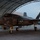 Lightning II strikes Iwakuni, F-35B arrives A U.S. Marine Corps F-35B Lightning II stealth fighter jet, marked with 'VMFA-121' (Marine Fighter Attack Squadron 121) and tail number '07', is being marshaled out of a large arched hangar structure during low-light conditions. Ground crew personnel are visible, with one marshal using green glow sticks to direct the aircraft. The aircraft's navigation lights are illuminated, suggesting it is powered up and preparing for taxi or departure.