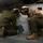 HMH-464 Marines Conduct Corrosion Prevention during Exercise Frigid Condor Two military personnel wearing flight helmets with goggles are crouching and inspecting or working on the exterior panel of a military aircraft. One individual is wearing an olive drab flight suit while the other is wearing a desert camouflage uniform. They appear to be conducting a maintenance check or pre-flight inspection on the aircraft's fuselage.