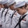 170117-N-BL637-115 A group of United States Navy sailors in dress white uniforms stand in a solemn formation with heads bowed, likely during a memorial or ceremonial event. The sailors display various ranks and service ribbons on their uniforms. The setting appears to be aboard a naval vessel with open water visible in the background.