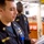 USS Lake Champlain (CG 57) CPO Advancement Exam Two U.S. Navy personnel are shown in what appears to be a shipboard interior space. The foreground sailor, identified by name tape as 'QUINTERO,' is reading a document and wears a Navy Chief Petty Officer collar insignia. A second sailor stands in the background, partially visible.