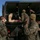 2d Medical Bn Field Exercise Military personnel in camouflage uniforms are loading a casualty on a stretcher into the back of a military vehicle. The scene appears to be a medical evacuation training exercise, as indicated by simulated wound makeup on the casualty. Multiple service members are coordinating the litter carry and vehicle loading procedure.