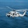 170118-N-NV908-069 A U.S. Navy military helicopter, identifiable as an MH-60 Seahawk variant, is captured in flight over open ocean waters. The aircraft is painted in standard naval gray and displays visible U.S. military markings including a star insignia and the number '6'. The rotors are in motion, and the helicopter appears to be on an active patrol or operational mission over blue ocean waters.