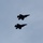 Lightning II strikes Iwakuni, F-35B arrives Two military fighter jets are flying in formation against an overcast gray sky. The aircraft appear to be fifth-generation stealth fighters, likely F-35s, based on their distinctive silhouette and delta-wing configuration. They are captured in a low-angle shot, appearing as dark silhouettes against the pale sky.