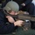 170118-N-BL637-097 A Navy personnel member in prone position is operating what appears to be an M240 machine gun during a training exercise. The individual is wearing standard protective gear including a ballistic helmet and safety glasses. Spent brass casings and ammunition are visible on the deck surface around the shooter.