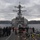 170123-N-JI086-200 A U.S. Navy Arleigh Burke-class guided-missile destroyer is shown from its bow deck, with crew members stationed on the forecastle in what appears to be a port arrival or departure evolution. The ship is navigating through a fjord or harbor with mountainous, snow-capped terrain visible in the background. Weather conditions are overcast and cold, consistent with a northern European or similar high-latitude location.