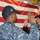 170120-N-BK708-952 Two U.S. Navy personnel are engaged in what appears to be a re-enlistment or oath-of-office ceremony, with one individual raising their right hand before an American flag. Both are wearing Navy Working Uniform (NWU) digital camouflage pattern uniforms and black caps. The ceremony is taking place aboard what appears to be a naval vessel, with additional personnel visible in the background.