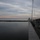 170120-N-OH262-496 A twilight or dusk scene photographed from the deck of a large vessel or ferry, looking out over calm water toward the horizon. A lone silhouetted figure stands on an upper deck railing, gazing toward the sea, while a rock breakwater extends along the left side. The sky displays soft pink and orange hues near the horizon beneath a layer of overcast clouds.