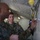2d Medical Bn Field Exercise Two military personnel in camouflage uniforms are inside what appears to be a field command tent or tactical operations center. The foreground individual is writing or marking on a whiteboard or map board using a blue marker, while a second service member observes attentively in the background. The setting suggests a military planning or briefing session.