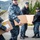 USS Bonhomme Richard (LHD 6) Sailors participate in a Food Drive Four military personnel in U.S. Navy blue digital camouflage (NWU Type I) uniforms are carrying cardboard boxes outdoors on a paved surface. They appear to be engaged in a logistics or humanitarian aid operation, with at least one box visibly bearing a DHL shipping label. The group appears in good spirits, with several members smiling.