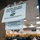 170119-N-OY799-057 A glass door or window displays two signs indicating the area is secured for a Navy-Wide Advancement Exam, directing people to find an alternate route. Through the glass, a large room is visible with numerous uniformed personnel seated at tables, actively taking the examination. A white Navy cover (hat) is visible on a table in the foreground.