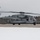 HMH-464 Marines Conduct Flight Operations during Exercise Frigid Condor A U.S. Marines heavy-lift helicopter, marked with the number '59' and 'MARINES' on its fuselage, is on a tarmac or runway surrounded by snow. The rotors are spinning, indicating the aircraft is powered up and likely preparing for takeoff or has just landed. The setting appears to be a cold-weather environment with snow-covered ground and bare trees in the background.