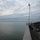 170120-N-OH262-553 The image shows the deck and bow area of a large vessel, likely a ferry or military ship, viewed from an elevated perspective looking forward over calm water. A mast with navigation lights and rigging lines is prominently visible, along with a small observation platform where one person is standing. The horizon shows a distant shoreline under a partly cloudy sky.