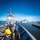 170116-N-BL607-371 U.S. Navy sailors in dark blue uniforms and safety helmets work on the deck of a warship during a port operation, likely a mooring or departure evolution. The foreground shows sailors handling lines and ropes, with a large gray naval cruiser or destroyer visible in the background. A harbor with additional vessels and a pier is visible, with numerous seagulls filling the sky.