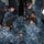 170117-N-DS065-0026 A group of U.S. Navy personnel in Navy Working Uniform (NWU) digital camouflage are gathered in a confined shipboard space conducting what appears to be a medical training drill or casualty care exercise. Multiple sailors are kneeling or crouching around a person lying on the deck, simulating emergency response procedures. One individual on the right edge of the frame holds papers, likely an observer or evaluator documenting the drill.