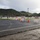 Camp Pendleton flood 2017 A wet road scene showing a closed entrance or access point blocked by multiple white and orange road barricades and traffic cones. The setting appears to be a commercial or industrial area with buildings, palm trees, and green hills visible in the background. The wet pavement and overcast sky suggest recent rainfall.