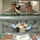 Two U.S. Air Force personnel in ABU (Airman Battle Uniform) camouflage are serving food in a military dining facility (DFAC). They are smiling at the camera while holding a divided meal tray containing rice, carrots, and a dark meat dish. The setting appears to be a standard military cafeteria-style serving line.
