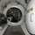 Army Divers plunge into the Pacific during exercise "Deep Blue" The image shows the interior of a hyperbaric chamber or decompression chamber facility, viewed through a circular pressure-sealed hatchway leading into a second inner chamber. The structure features thick cylindrical pressure vessel walls with polished metal hatch rings, brass valves, and various life-support and monitoring equipment. The diamond-plate steel flooring and multiple interconnected chambers suggest a multi-lock diving or medical hyperbaric system.