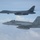 170214-N-XZ522-004 Two U.S. military aircraft are flying in formation over a cloud-covered sky. The upper aircraft is a U.S. Air Force B-1B Lancer strategic bomber with tail code 'DY' and number '1103', while the lower aircraft is a U.S. Navy F/A-18E/F Super Hornet marked '303' from squadron VFA-192 with tail code 'NE'. This appears to be a joint Air Force and Navy formation flight, likely over the Pacific region.