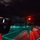 170212-N-HI376-520 A nighttime naval flight deck operation showing a military helicopter landed on a ship's deck, illuminated by red and green lighting. Personnel in flight deck gear are visible managing the operation, with one crew member in the foreground wearing a yellow helmet and headset. The dramatic low-light photography captures the atmospheric conditions of an at-sea night operation.