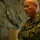 Lt. Gen. Nicholson recognizes Airmen’s support in MV-22 incident A senior military officer in MARPAT (Marine pattern) digital camouflage uniform stands with arms crossed, appearing to be listening or observing. Rank insignia visible on the collar suggests a high-ranking officer. The setting appears to be an indoor military facility with a textured stone or rock-climbing wall in the background.
