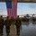 MAG-29 Change of Command A formal military ceremony is taking place inside a large aircraft hangar, with personnel in camouflage uniforms standing at attention before a large American flag. The ceremony appears to be a change of command or similar official military event, with troops assembled in formation. Large military helicopters, identifiable as CH-53 variants, are visible outside the open hangar bay doors at dusk.