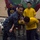 Dwight D. Eisenhower A U.S. Navy instructor in NWU (Navy Working Uniform) digital camouflage is demonstrating a defensive tactics or combatives technique on a trainee wearing a yellow 'NAVY' PT shirt. Several other Navy personnel in PT gear observe the demonstration in what appears to be a training facility or gymnasium aboard a ship or base. The scene depicts a formal military hand-to-hand combat or self-defense training session.