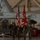 MAG-29 Change of Command A U.S. Marine Corps color guard stands at attention inside a military aircraft hangar, holding the U.S. national flag and the Marine Corps flag. Four Marines in woodland MARPAT camouflage uniforms are positioned in a formal ceremonial formation, with two armed rifle bearers flanking two flag bearers. The setting appears to be an official military ceremony conducted within a hangar containing what appears to be a large military aircraft.