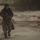 In the CRRC of Time: U.S. Marines and Japanese Soldiers conduct Recon Drills at Exercise Iron Fist A single armed military or special operations personnel is moving across a sandy beach environment, carrying a rifle with what appears to be a bayonet or suppressor attached. The individual is wearing camouflage uniform, a black helmet, and tactical gear, and appears wet or muddy, suggesting recent water operations. The beach setting includes sand dunes, scattered debris, driftwood, and shallow water pools in the background.