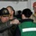 Nimitz Sailors undergo inspection A military officer wearing a 'Board of Inspection and Survey' cap is pinning or attaching something to the collar/shoulder area of a person in a green work vest with a reflective stripe. Several other individuals are present in the background, including one wearing a bright orange camouflage cap. The setting appears to be aboard a naval vessel or military facility.