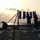 170215-N-JI086-016 The image shows silhouetted personnel on what appears to be a naval vessel's flight deck or helicopter landing pad at sunset or sunrise. Several crew members are setting up a frame structure with blue target panels or shooting targets hanging from a line strung between two posts. The scene is backlit by a hazy sun over open ocean water.