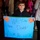 SPMAGTF-CR-CC returns from deployment A young boy holds a handmade blue poster board sign welcoming his father home, likely from military deployment. The sign reads 'Welcome Home Daddy You're My HERO!' and is decorated with orange paper hearts and green glitter tape. The setting appears to be an indoor gathering with multiple people visible in the background.