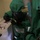 Chemical, Biological, Radiological and Nuclear Marines Participate Advanced Training Two individuals are wearing green full-body hazmat/chemical protective suits in what appears to be an indoor training environment. The central figure is handling a small instrument or sample device with black-gloved hands. A label on the suit clearly reads 'TRAINING SUIT ONLY,' confirming this is a training exercise.