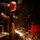 Nimitz Sailor tests PECU A welder is actively working in an industrial workshop, using a welding torch on a metal workpiece that is producing a bright shower of sparks. The worker is wearing appropriate personal protective equipment including a red welding helmet and heavy-duty gloves. The workshop environment is well-equipped with visible tool storage, welding machines, and cables in the background.