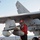 GHWB is the flagship of Carrier Strike Group (CSG) 2, which is comprised of the staff of CSG-2; GHWB; the nine squadrons and staff of Carrier Air Wing (CVW) 8; Destroyer Squadron (DESRON) 22 staff and guided-missile destroyers USS Laboon (DDG 58) and USS A U.S. Navy ordnanceman wearing a red jersey and helmet marked '4W' is handling munitions mounted under the wing of a carrier-based aircraft, identifiable by tail number 410. The scene takes place on the flight deck of an aircraft carrier at sea, with the ocean visible in the background. The sailor appears to be inspecting or loading weapons onto the aircraft's underwing hardpoints.