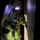 Chemical, Biological, Radiological and Nuclear Marines Participate Advanced Training A person is wearing a full hazmat/CBRN (Chemical, Biological, Radiological, Nuclear) protective suit in a dark environment. The suit is lime/yellow-green in color with a reflective visor and appears to be a Level A or Level B encapsulated protective ensemble. The individual appears to be entering or exiting through a doorway or hatch, with a light source illuminating the scene from the right side.