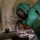 Chemical, Biological, Radiological and Nuclear Marines Participate Advanced Training A person wearing full hazmat/chemical protective gear including a green encapsulating suit and black gloves is working with laboratory glassware on a countertop. The individual appears to be conducting a chemical procedure involving a round-bottom flask mounted on a stand with tubing connections. The setting appears to be a confined indoor space, possibly a bathroom or small room converted for this activity.