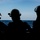 Dwight D. Eisenhower The image shows four individuals in silhouette, facing away from the camera toward an open body of water. All subjects are wearing helmets equipped with communication headsets and visors, suggesting a military or naval operational context. The strong backlight from the horizon creates a dramatic high-contrast silhouette effect.