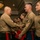 CMC awards Reserve Career Planner of the Year A formal U.S. Marine Corps awards or recognition ceremony taking place in what appears to be a hotel ballroom or conference facility. A senior officer (wearing no visible rank insignia on collar but dressed in Service 'C' uniform with red-striped trousers) is shaking hands with a Staff Sergeant while holding a red award folder. Multiple Marines in Service uniform are lined up in the background awaiting their turn.