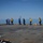 170214-N-NJ910-0142 A group of approximately seven naval personnel are standing on what appears to be a flight deck of a military vessel at sea. The crew members are wearing color-coded safety vests (yellow and blue), which are standard on carrier flight decks to denote different roles. One individual has their arm raised, possibly signaling or communicating with others.