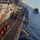 170214-N-NJ910-0121 An aerial/elevated view of a naval vessel's deck during what appears to be an underway replenishment (UNREP) operation at sea. Personnel wearing orange life vests and red jackets are visible on the deck, with transfer lines and rigging extending toward a second vessel visible in the background. The operation is taking place in calm, open blue water under clear conditions.