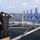 170215-N-JI086-065 Military personnel, likely U.S. Navy sailors, are conducting a pistol qualification exercise on the deck of a naval vessel at sea. Several individuals in dark uniforms are aiming handguns at blue silhouette paper targets suspended from a wooden frame. The exercise appears to be a standard small arms qualification drill conducted on an open ocean backdrop.